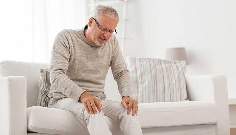 old man holding sore knee on couch